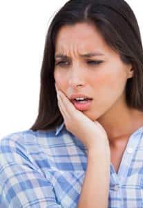 Woman in blue checkered shirt holding cheek, expressing tooth pain or discomfort against white background.