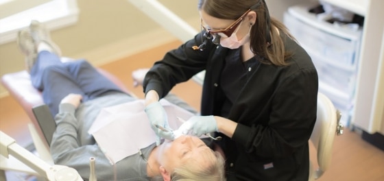 Dentist in black gloves examining patient's teeth in dental office treatment chair.