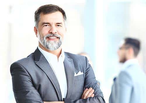 Professional man in business suit smiling with arms crossed in modern office setting.