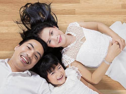 Family of three lying on wooden floor, smiling at camera in relaxed pose.
