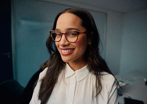 Smiling woman wearing glasses and white shirt in modern dental office setting