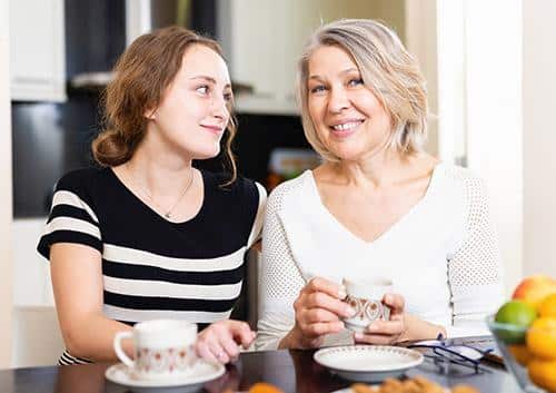 Two women smiling while sharing a meal together in a bright kitchen setting.