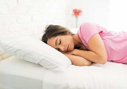 Woman sleeping peacefully on white bed pillow in pink shirt