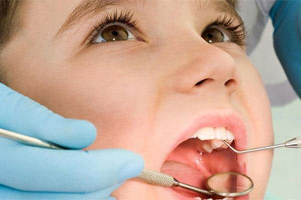 Child receiving dental examination with dentist's tools and gloved hands in clinical setting.