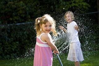 Two young children playing with water hose on sunny summer day in backyard garden.