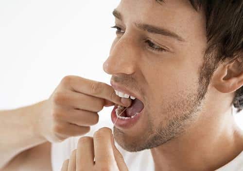Man flossing teeth against white background, demonstrating proper dental hygiene