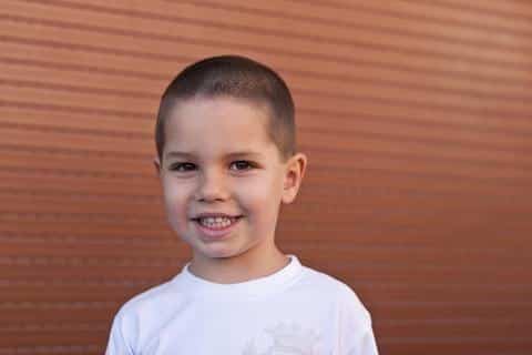 Young child smiling at camera wearing white shirt against orange corrugated background.