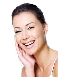 Smiling woman with clear skin touching her face against white background, dental care promotion.