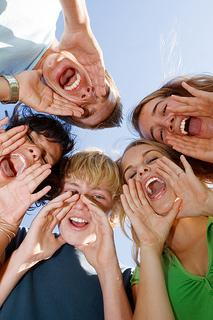 Group of smiling children looking down at camera with hands forming circle, outdoor setting.