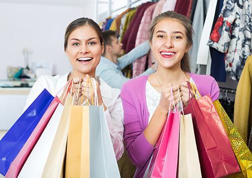 Two smiling women holding shopping bags in a retail clothing store.