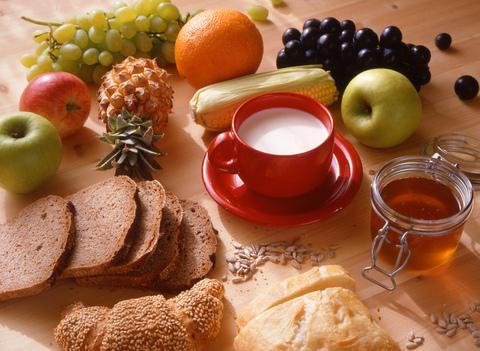 Healthy foods arranged on wooden surface: fruits, vegetables, bread, and milk for dental health nutrition.