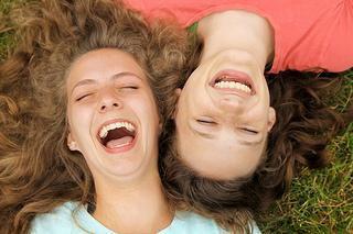 Two young people lying on grass laughing and smiling together outdoors.