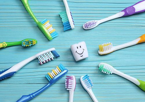 Colorful toothbrushes arranged in circle around smiling tooth character on blue wooden surface.