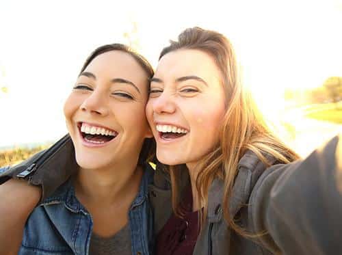 Two women smiling together outdoors taking a selfie during golden hour.