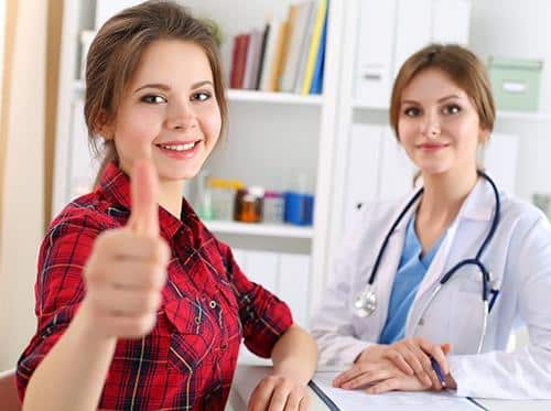 Patient giving thumbs up during dental consultation with female dentist in clinical office setting.