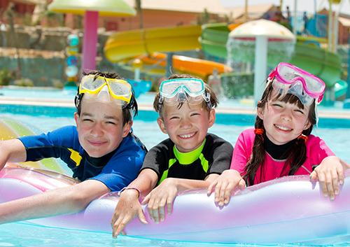 Three children wearing goggles in a swimming pool at a water park facility.