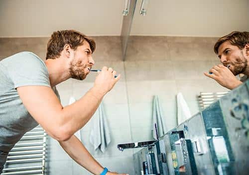 Man brushing teeth at bathroom mirror in morning routine.