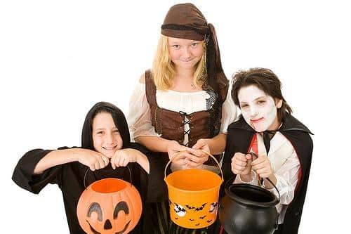 Four children in Halloween costumes holding jack-o'-lantern candy buckets against white background.