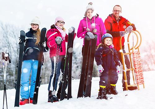 Family of six enjoys winter sports activities together in snowy mountain setting.