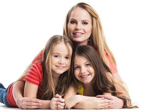 Woman with two young girls smiling together in studio portrait setting.