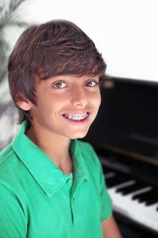 Smiling young boy in green shirt posing by piano keyboard indoors.