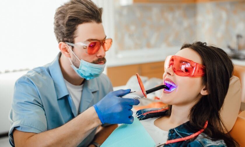 Dentist applying purple LED whitening treatment to patient's teeth during Zoom whitening procedure.