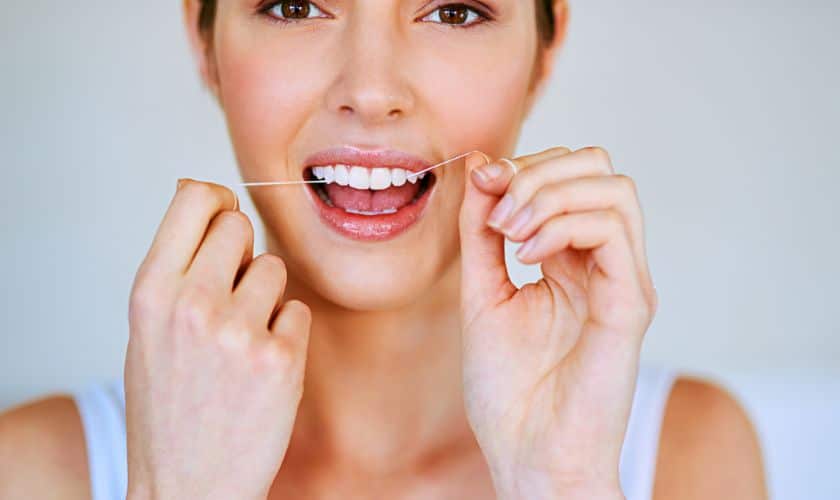 Woman smiling while flossing teeth against light blue background