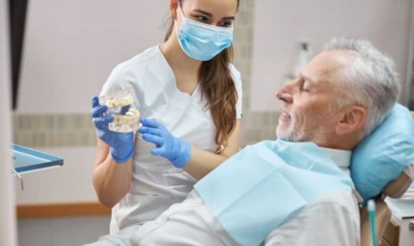 Dentist showing dental implant model to senior male patient in Fayetteville dental office.