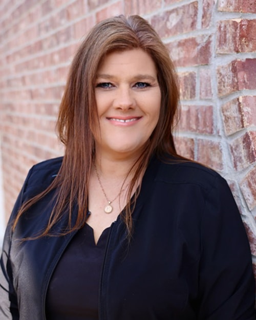 Professional woman smiling at camera against brick wall background for dental practice portrait