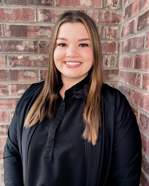 Young woman smiling at camera wearing black shirt against brick wall background.