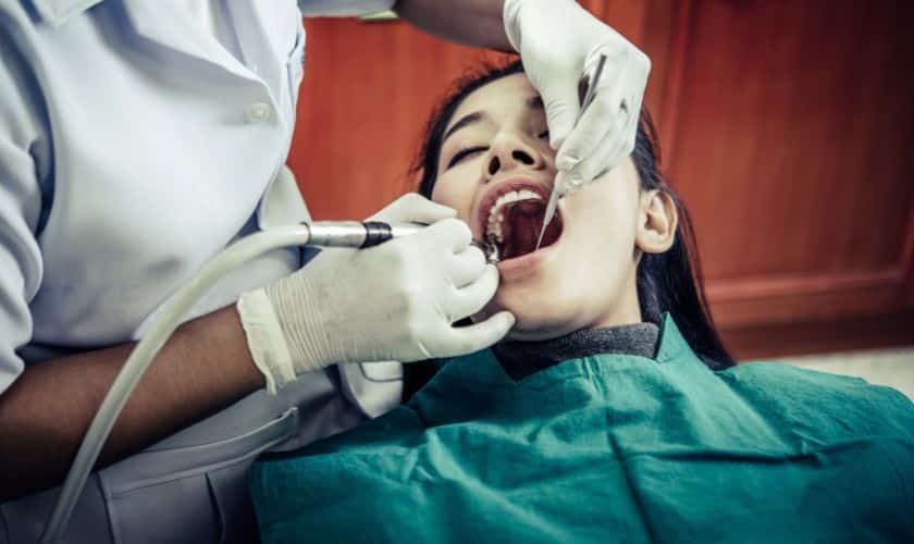 Dentist examining patient's teeth during dental procedure in treatment chair.