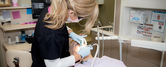 Dental professional examining patient's teeth in modern dental office treatment room.
