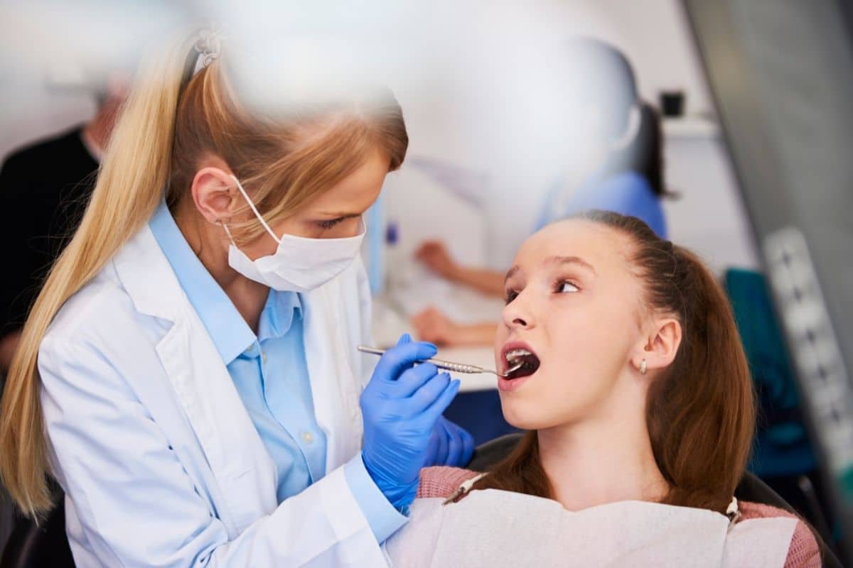 Dentist in mask and gloves examining young patient's teeth in dental office.