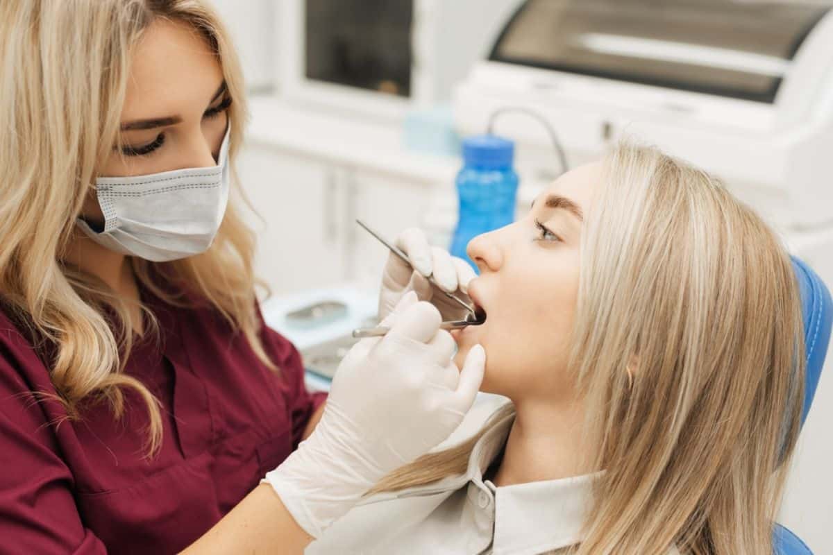 Dental hygienist in mask examining patient's teeth in modern dental office setting.