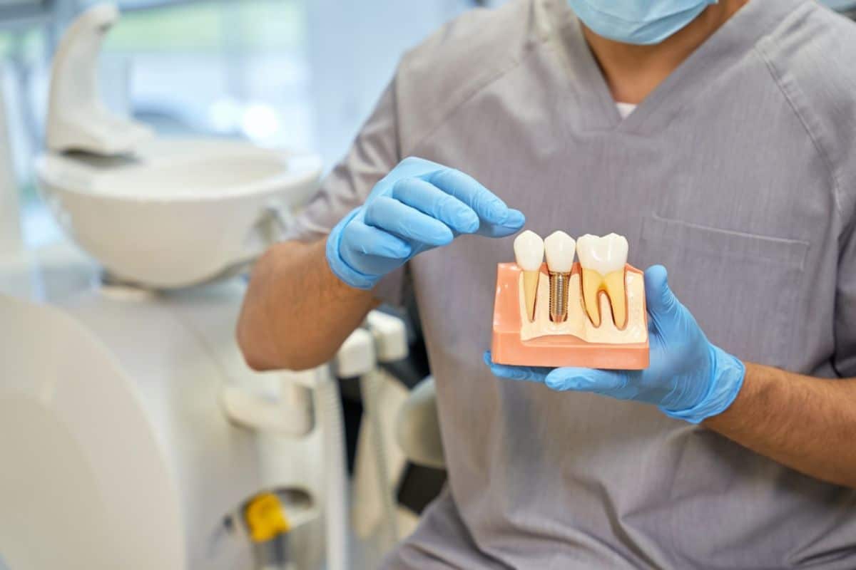 Dental professional in gloves holding tooth shade guide samples in clinical setting.