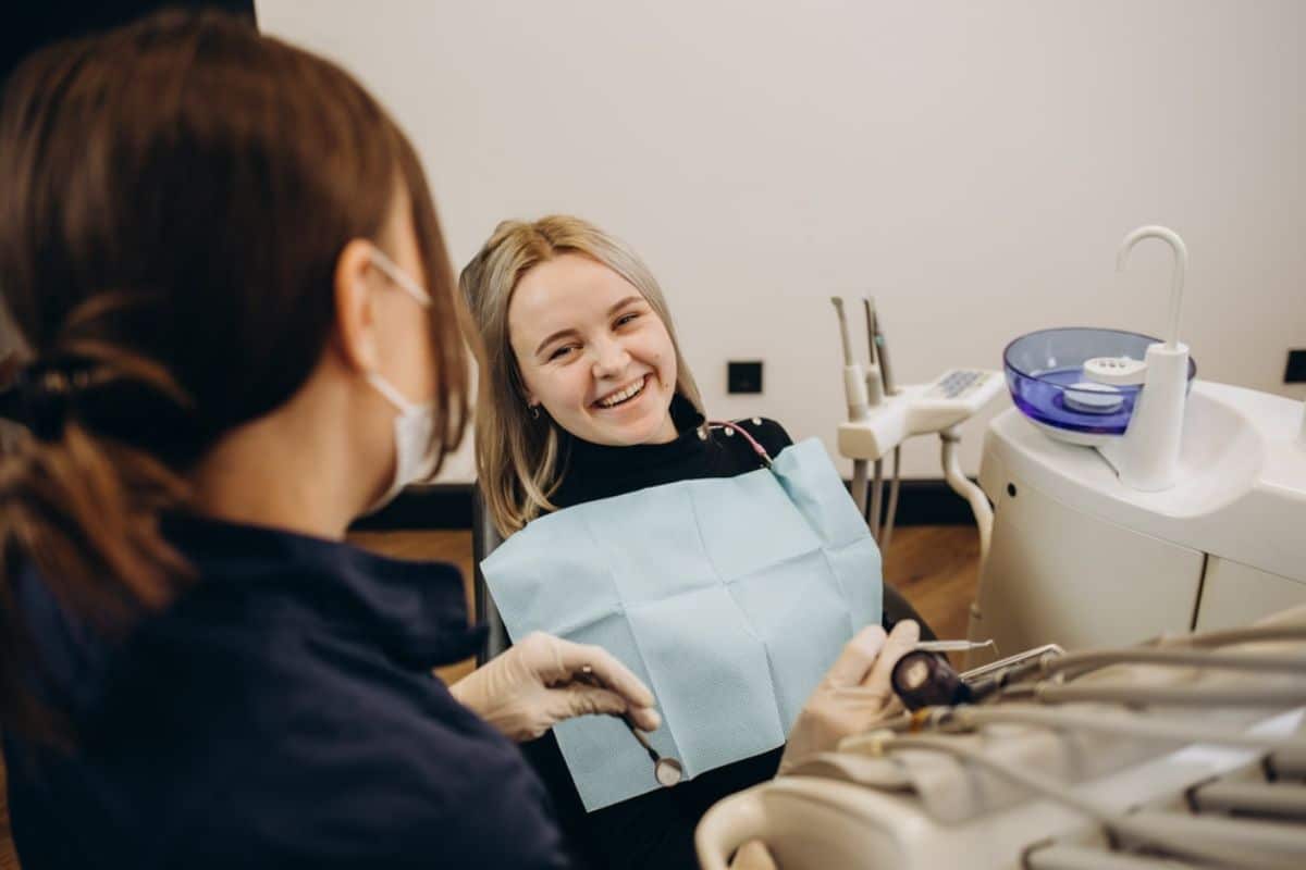 Dental patient in chair receiving examination from female dentist in clinical office setting.