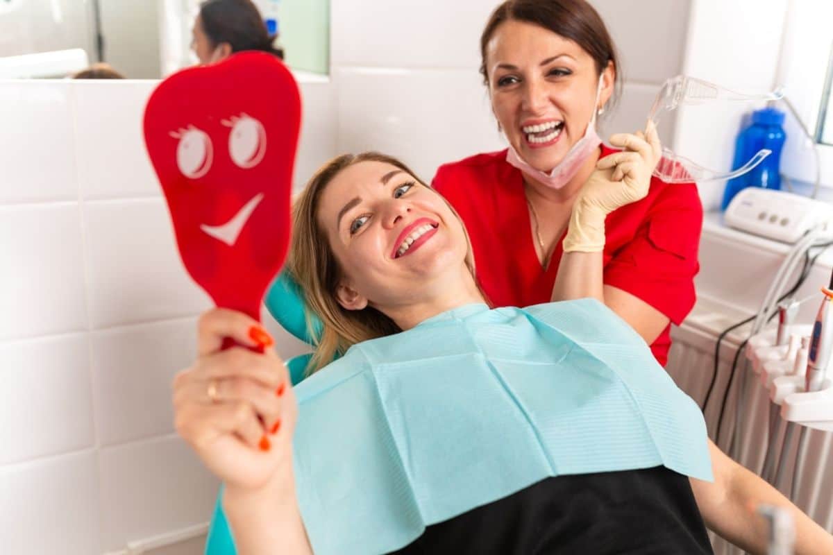 Pediatric dentist showing smiling smiley face tool to child patient in dental office chair.