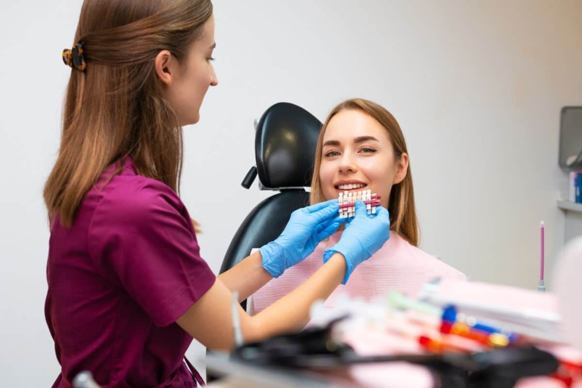 Dental professional fitting blue protective gloves while patient sits in dental chair.