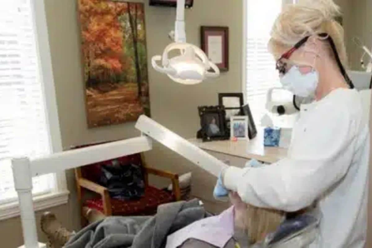Dentist in white coat and mask examining patient in modern dental office treatment room.