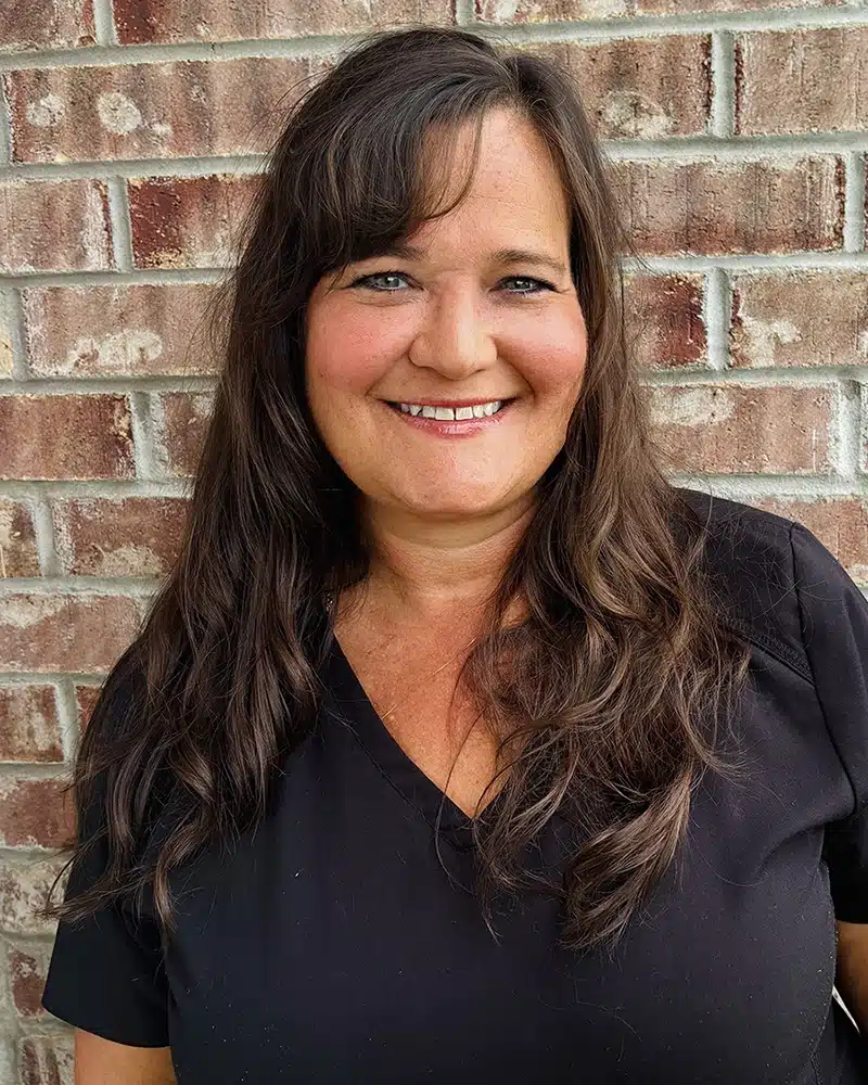 Professional woman smiling at camera against brick wall background for dental practice.