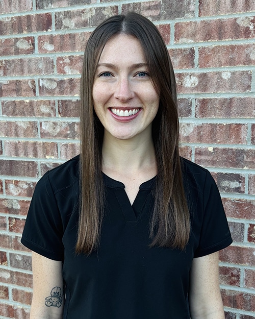Woman smiling at camera wearing black polo shirt against brick wall background.