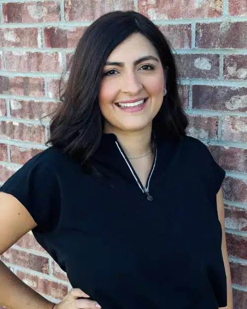 Woman smiling at camera wearing black shirt against brick wall background