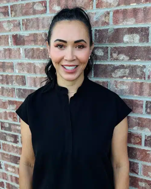 Woman smiling at camera wearing black shirt against brick wall background.